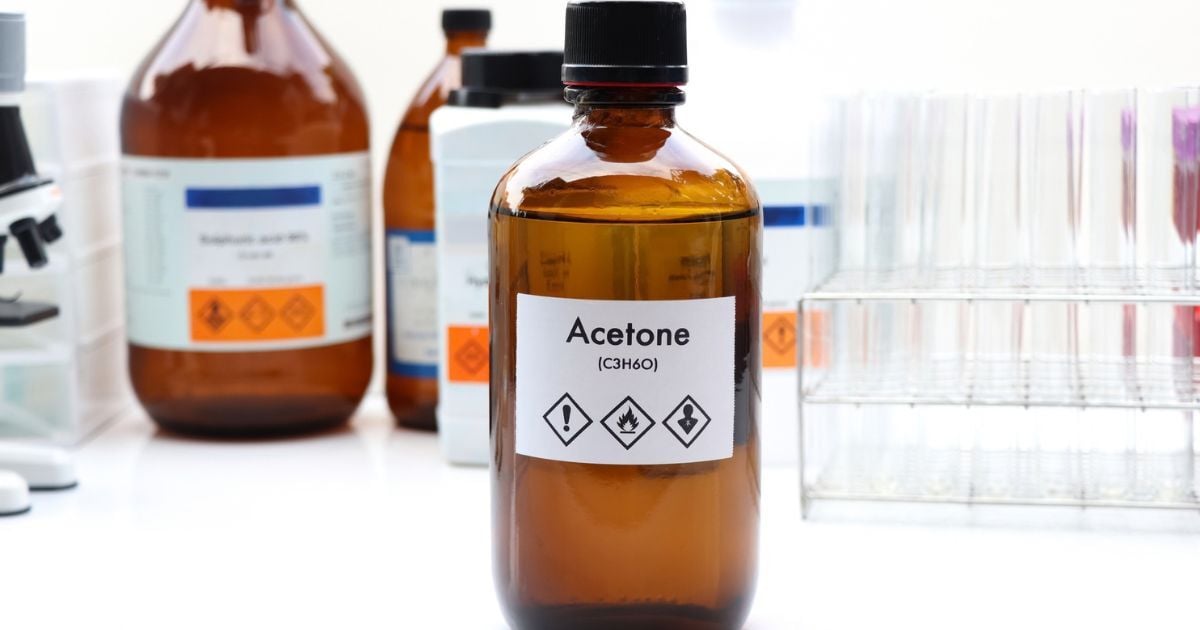 A brown bottle of acetone sitting on a white lab table.