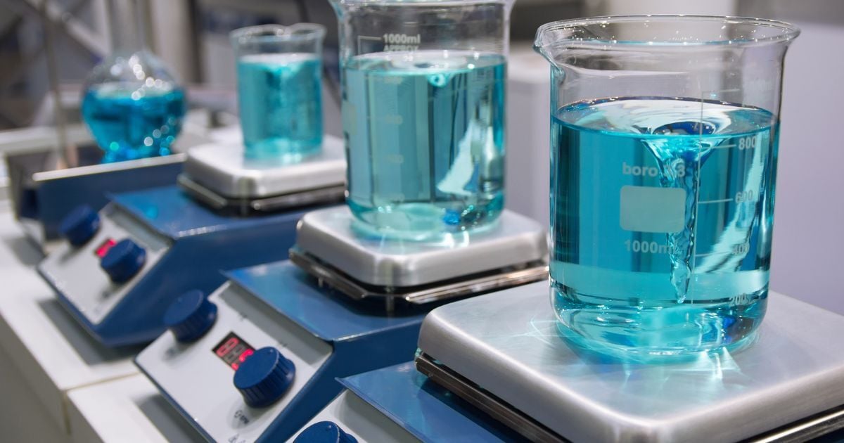 Several magnetic mixers in a lab holding flasks filled with blue liquid.