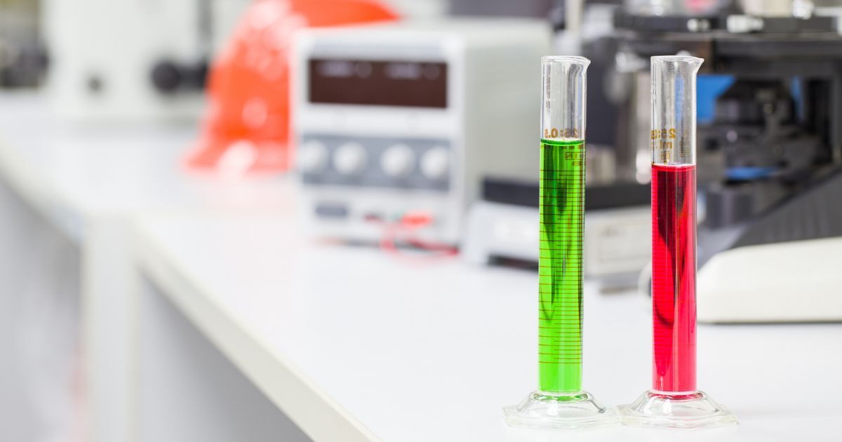 Two graduated cylinders filled with different colored liquids on a benchtop.