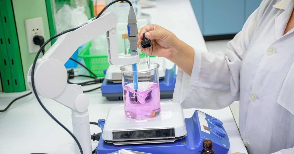 A scientist dropping liquid into a beaker on a magnetic stirrer.