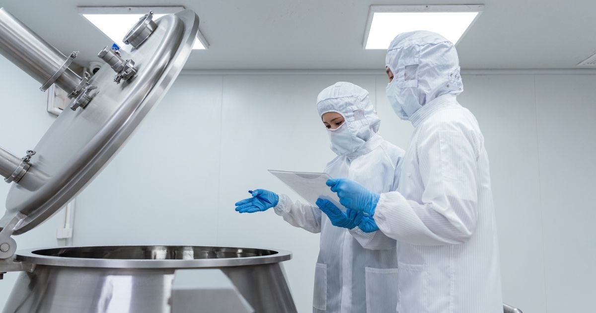 Lab techs in protective suits examine a large lab mixer.