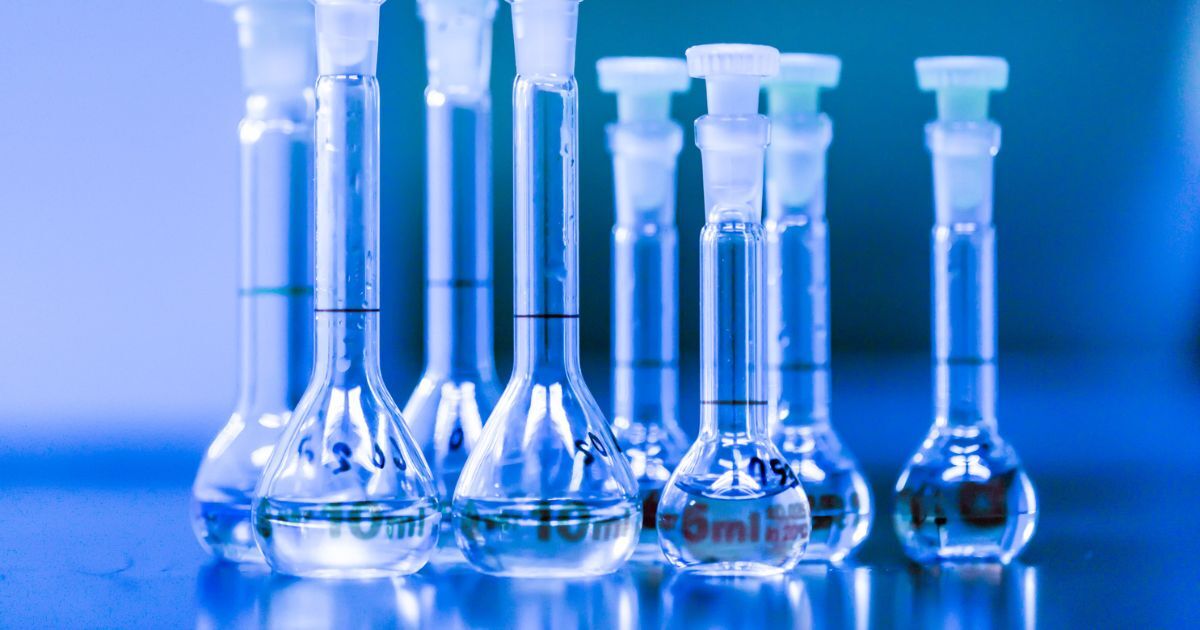 Several volumetric flasks on a tabletop against a blue background.